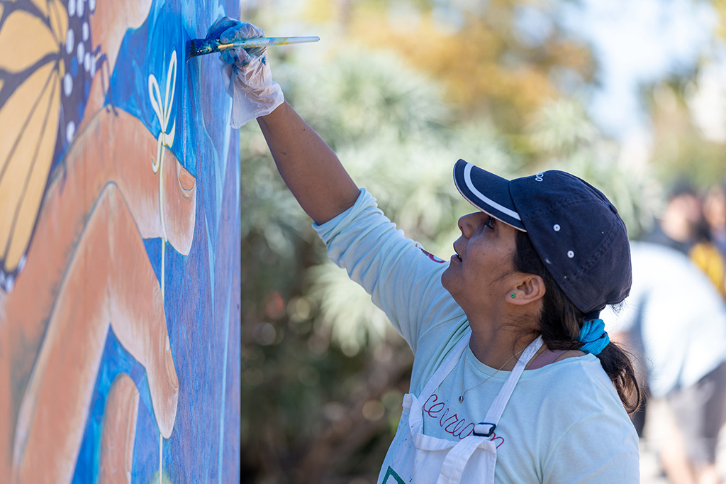 An artist paints a colorful mural on an outdoor wall.