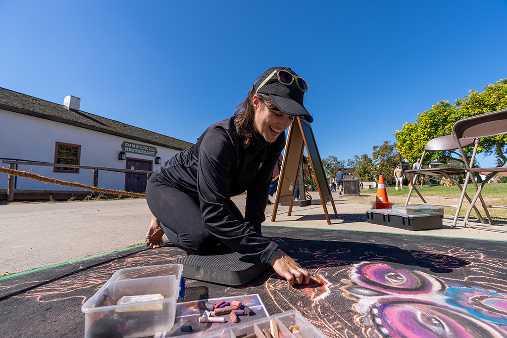 An artist kneels on the pavement drawing colorful chalk art.