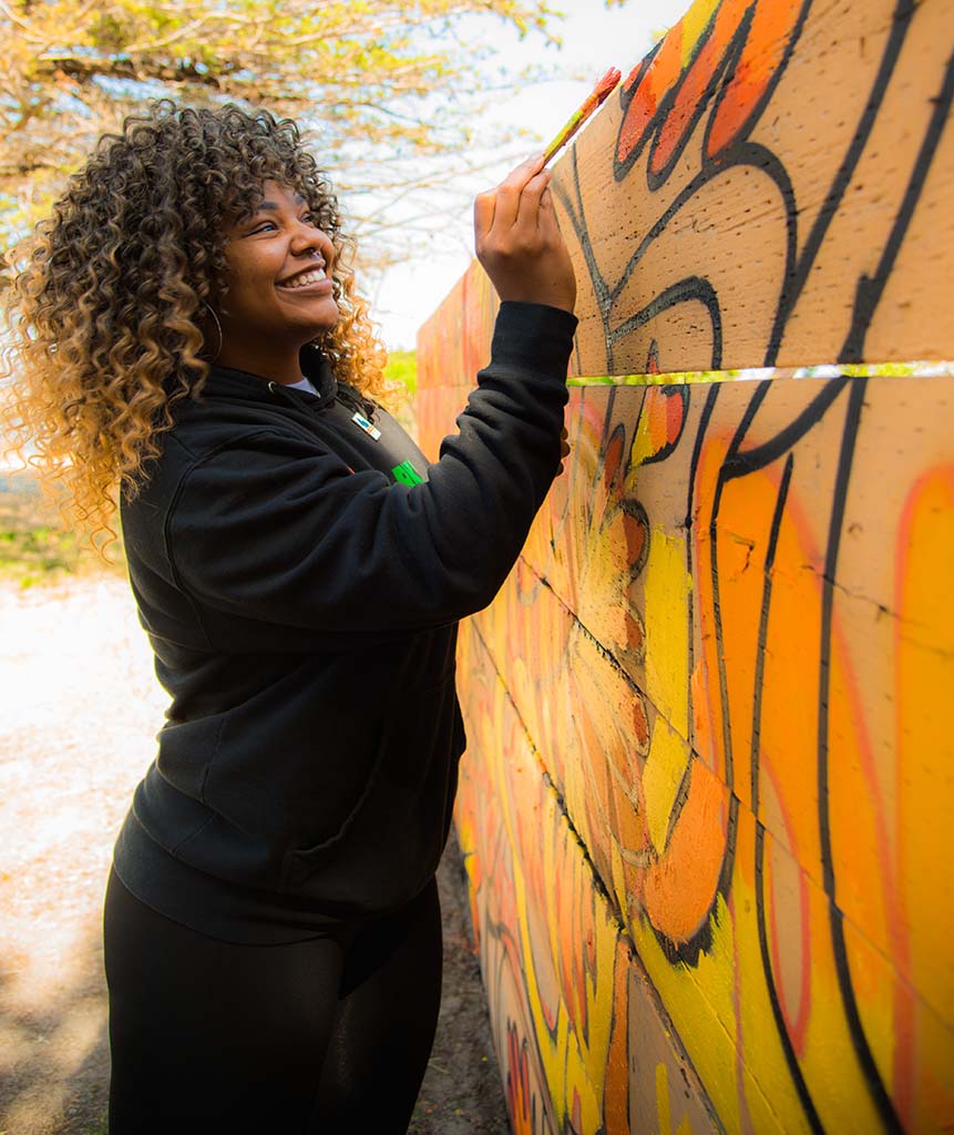A person paints part of a colorful outdoor mural.